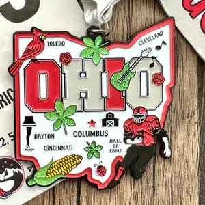 May include: A red, white, and gray metal Ohio state outline medal with a red cardinal, a guitar, a football player, and other state-specific icons. The medal says "OHIO" in large letters.