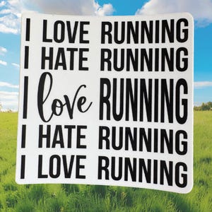 May include: A white square sign with the phrases "I LOVE RUNNING", "I HATE RUNNING", and "I love RUNNING" in black text. The sign is set against a backdrop of green grass and a blue sky.