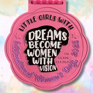 May include: A pink medal with the text "Little Girls With Dreams Become Women With Vision" and "International Women's Day 2026". The medal has a ribbon with a heart pattern.