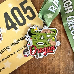 May include: A green and white ribbon with the text "Race Oregon" and a metal medal featuring a map of Oregon with various landmarks and the text "Oregon". The medal is attached to the ribbon. The number "405" is visible on a yellow background.