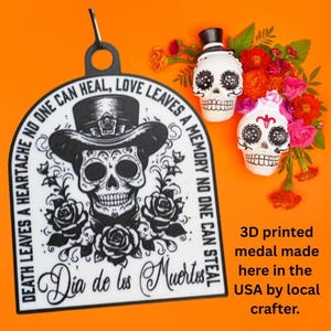 May include: A Dia de los Muertos themed 3D printed medal with a skull wearing a hat and roses. The medal has the text "DEATH LEAVES A HEARTACHE NO ONE CAN HEAL, LOVE LEAVES A MEMORY NO ONE CAN STEAL". Two skull figurines and flowers are also in the image.