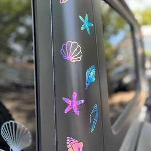 May include: A black car with a row of iridescent stickers on the side. The stickers are of seashells and a starfish. The stickers are all different colors and have a holographic finish.