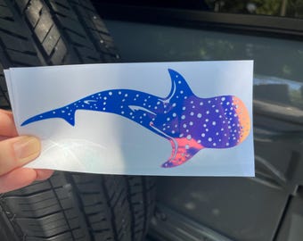 Op de afbeelding: Een blauwe en paarse iriserende walvishaai-sticker met witte stippen. De sticker is op een witte achtergrond.