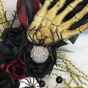 May include: A Halloween wreath with black roses, a skeleton hand, a spider with a sparkly body, and white pumpkins with black spiderwebs.