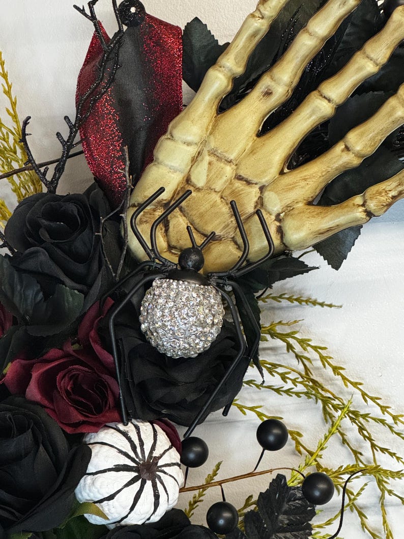 May include: A Halloween wreath with black roses, a skeleton hand, a spider with a sparkly body, and white pumpkins with black spiderwebs.
