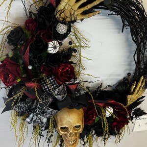 May include: A black and red Halloween wreath with a skull, skeleton hands, and black roses.
