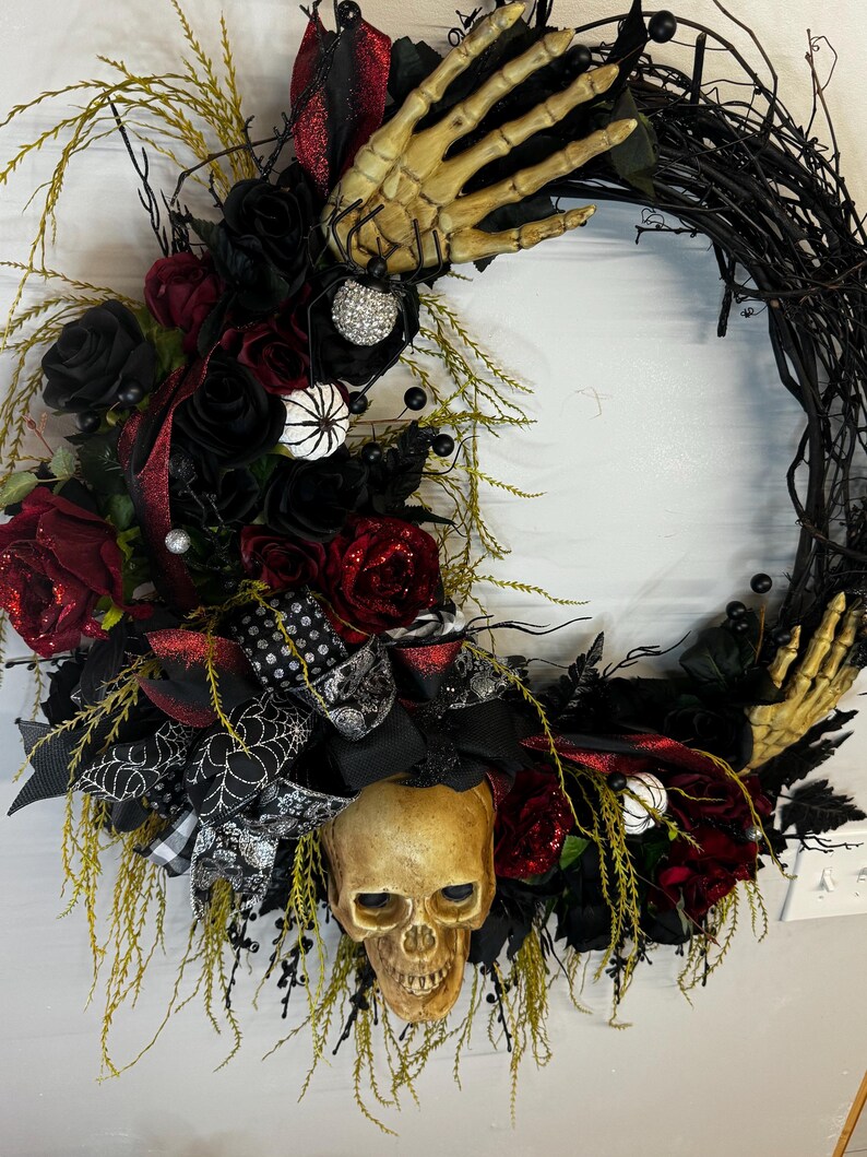 May include: A black and red Halloween wreath with a skull, skeleton hands, and black roses.