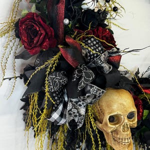 May include: A black and red Halloween wreath with a skull, black roses, and a black and white checkered ribbon.