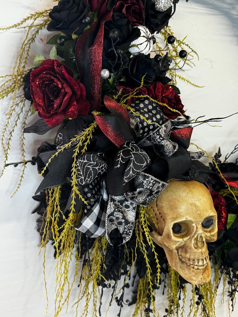 May include: A black and red Halloween wreath with a skull, black roses, and a black and white checkered ribbon.