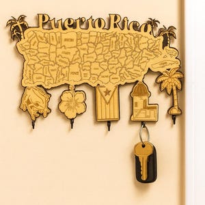 May include: Wooden key holder shaped like the island of Puerto Rico, with the name "Puerto Rico" at the top. Features a map of the island with key hooks below, and decorative elements like a frog, flower, flag, building, and palm trees.