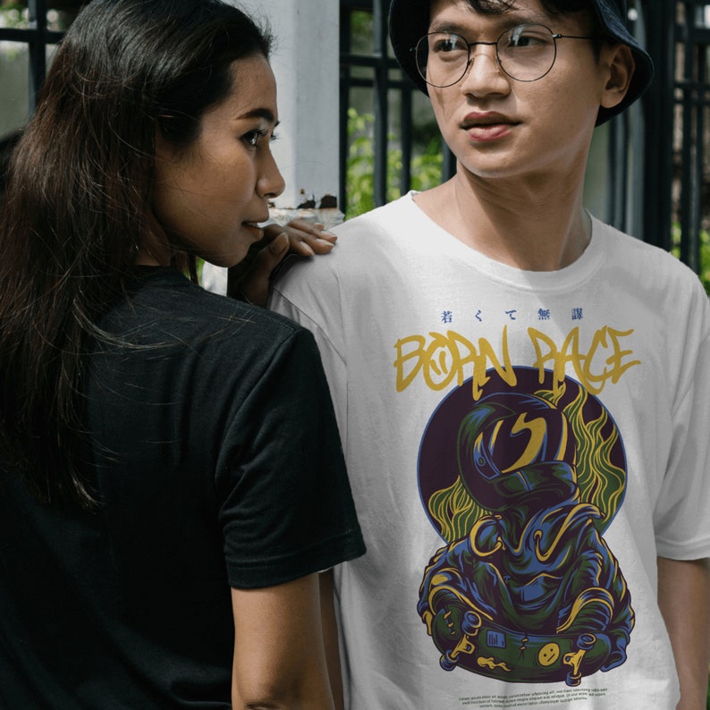 May include: White t-shirt with a graphic of a person wearing a helmet and riding a skateboard. The graphic is in blue, yellow, and black. The text "Born Rage" is written in yellow and black on the shirt.