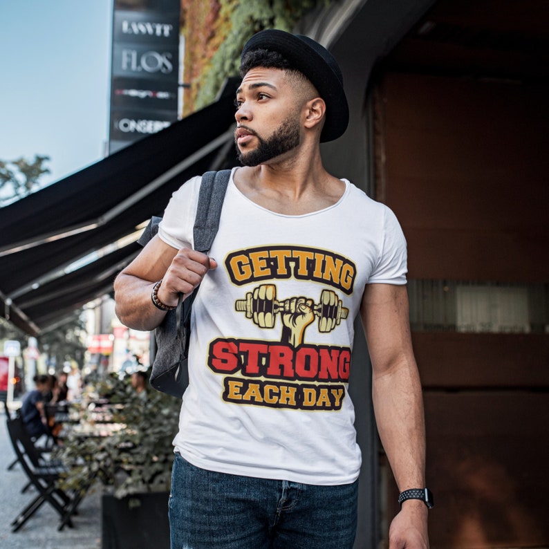 May include: White t-shirt with a graphic of a hand lifting a dumbbell. The graphic has the text "GETTING STRONG EACH DAY" in yellow, red, and black.