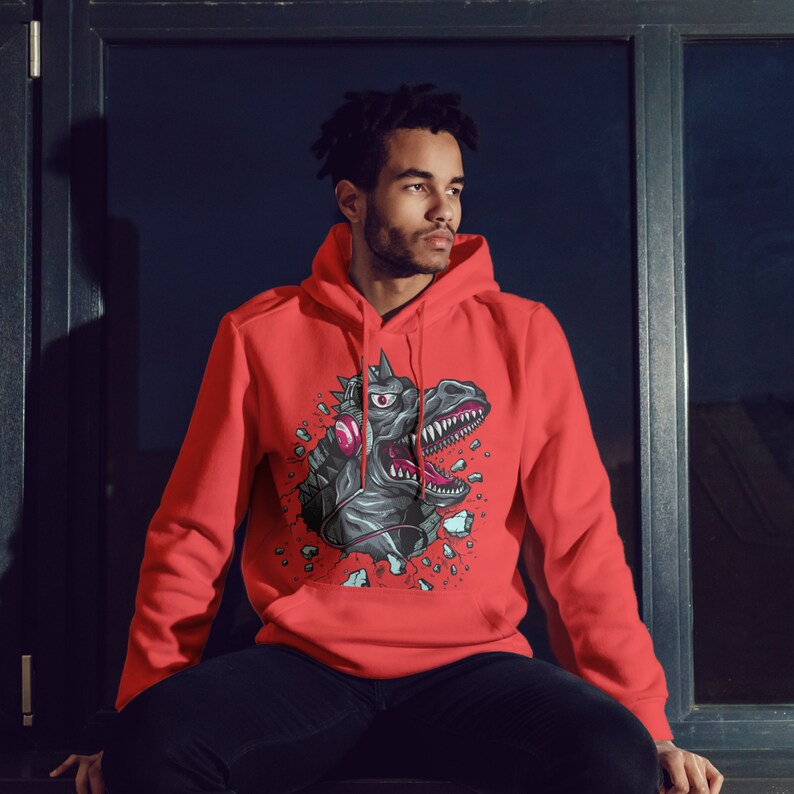 May include: A red hoodie with a graphic of a dinosaur wearing headphones and breaking through a wall. The dinosaur is gray and has a pink eye.