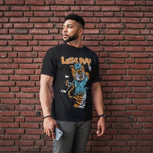 May include: A black t-shirt with a graphic of a tiger wearing a golf hat and holding a golf club. The text "Let's Play" is printed on the shirt.