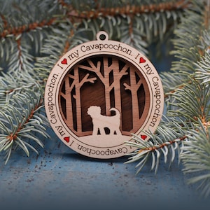 May include: A wooden Christmas ornament with a silhouette of a dog in a forest scene. The ornament is decorated with the text "I love my Cavapoochohn" on both sides.