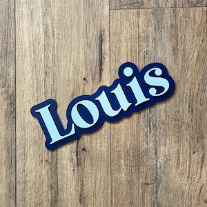 May include: A blue and white wooden sign with the name "Louis" in a bold, stylized font.
