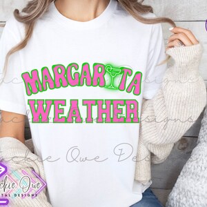 May include: A white t-shirt with the text "Margarita Weather" in pink letters with a green outline. A green margarita glass icon is above the word "Margarita".