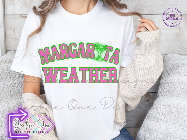 May include: A white t-shirt with the text "Margarita Weather" in pink letters with a green outline. A green margarita glass icon is above the word "Margarita".