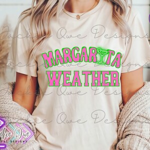 May include: A white t-shirt with the text "Margarita Weather" in pink letters with a green outline. The text is in a retro font style.