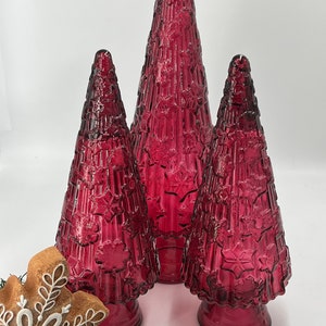 May include: Three red glass Christmas trees of varying sizes. The trees are decorated with a snowflake pattern and have a textured surface.