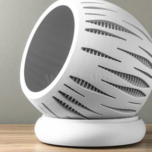 May include: A white, spherical decorative object with a large opening and a series of horizontal, cut-out lines. The object sits on a rounded base, creating a modern, minimalist design. The interior is a darker shade of gray.