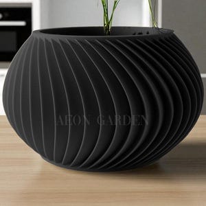May include: A black, spherical planter with a spiral ribbed design. The planter has the text "AEON GARDEN" printed on the front. The planter is sitting on a wooden surface and contains green plants.