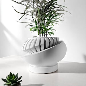 May include: A modern white planter with a unique geometric design, holding a lush green plant. The planter has a spherical base and a segmented top, creating a striking contrast. A small succulent is in the foreground.