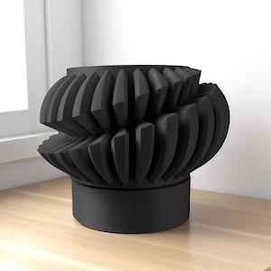 May include: A black, abstract sculpture with a unique, layered design. The sculpture features a cylindrical base supporting a complex, geometric form with repeating, angled elements. The piece is displayed on a light-colored wooden surface.
