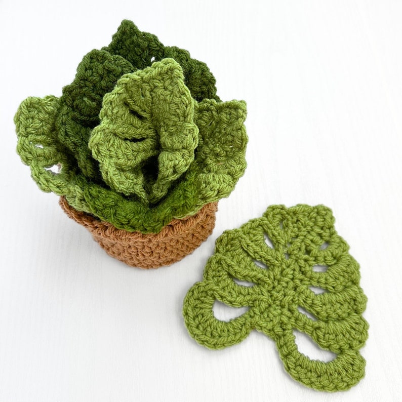 May include: A crocheted potted plant with green leaves and a brown pot. A separate green crocheted leaf is also shown.