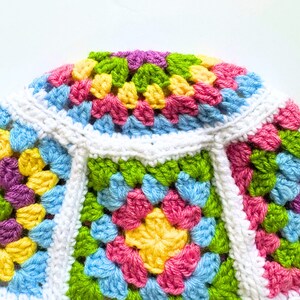 May include: A colorful crocheted granny square blanket with a white border. The blanket is made with different shades of pink, blue, green, and yellow yarn.