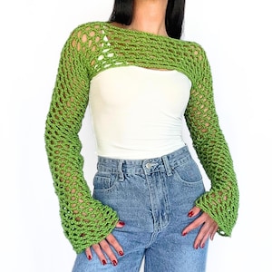 May include: A green crochet shrug with long sleeves and a wide, open neckline. The shrug is made with a delicate, open stitch pattern.