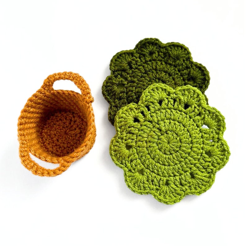 May include: A set of three crocheted coasters in shades of green and orange. The coasters are round and have a scalloped edge. The coasters are perfect for adding a touch of handmade charm to your home decor.