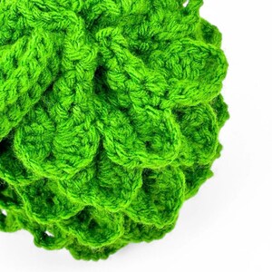 May include: A bright green crocheted sphere featuring a textured, layered scale-like pattern created with yarn. The object has a rounded, three-dimensional shape with visible interlocking stitches throughout the entire surface of the item.
