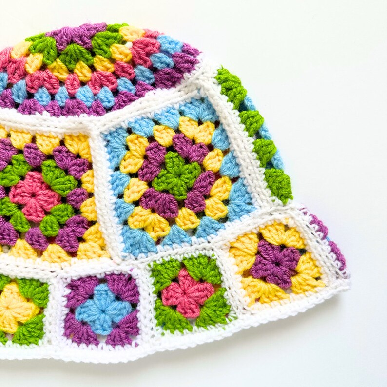 May include: A colorful crocheted hat with a white brim and a pattern of squares in shades of pink, yellow, green, blue, and purple.