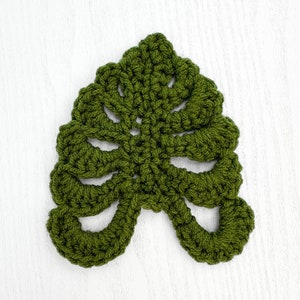 May include: A green crocheted leaf with a detailed design. The leaf is made with a single crochet stitch and has a delicate, lacy appearance.