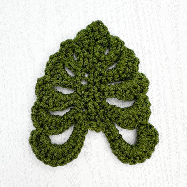 May include: A green crocheted leaf with a detailed design. The leaf is made with a single crochet stitch and has a delicate, lacy appearance.