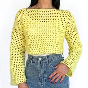Può includere: Un maglione di uncinetto giallo con una scollatura ampia e aperta e maniche lunghe. Il maglione ha un design a maglia larga e aperta.