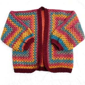 May include: A colorful crocheted cardigan with a striped pattern in shades of burgundy, orange, yellow, blue, and gray. The cardigan has a long, open front and long sleeves.