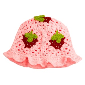 K&ouml;nnte beinhalten: Ein rosa geh&auml;kelter Bucket-Hut mit drei gestickten Erdbeeren. Die Erdbeeren sind rot mit gr&uuml;nen Bl&auml;ttern.