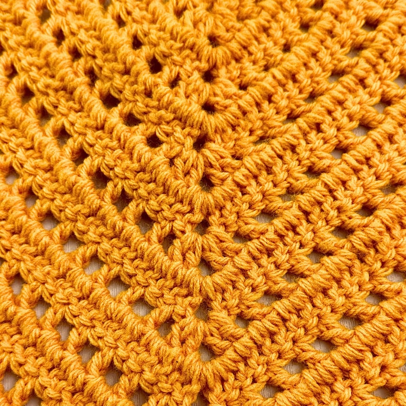 Puede incluir: Primer plano de una tela de crochet con un patr&oacute;n repetitivo de cuadrados y diamantes. La tela es de color naranja oscuro.