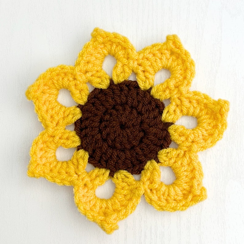 Peut inclure: Un tournesol crochet&eacute; avec un centre brun et des p&eacute;tales jaunes. Le tournesol est fait de fil et a un aspect textur&eacute; et fait main.