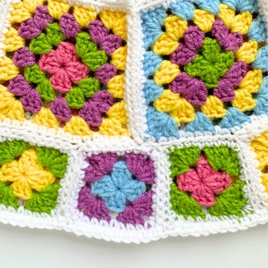 May include: A crocheted blanket with a colorful granny square pattern. The squares are made in shades of yellow, green, pink, blue, and purple.
