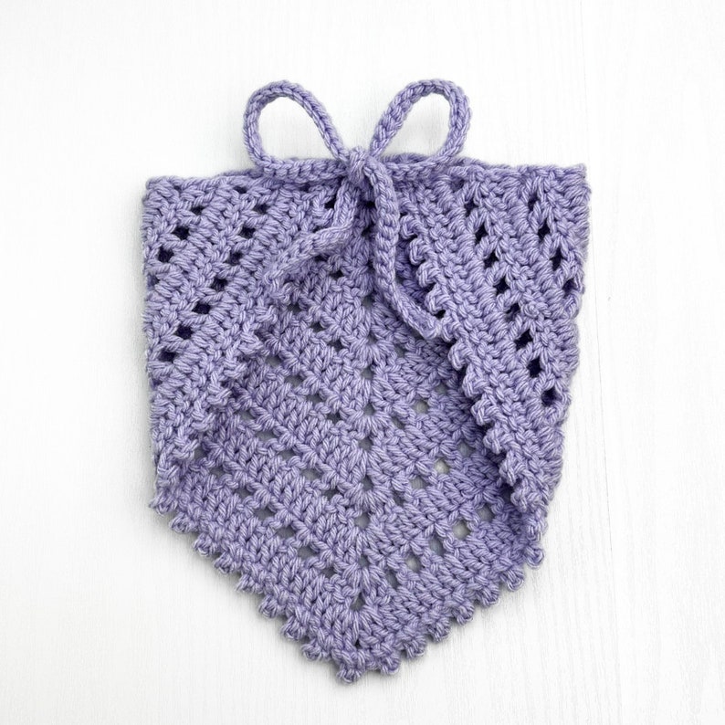 Puede incluir: Una bufanda de cuello de ganchillo de color lavanda con un lazo. La bufanda tiene un patr&oacute;n delicado y de encaje.