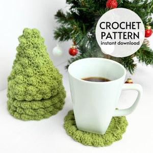 Puede incluir: Posavasos de crochet verde en forma de árbol de Navidad con una taza blanca y café encima. El texto "CROCHET PATTERN instant download" está en un círculo blanco.