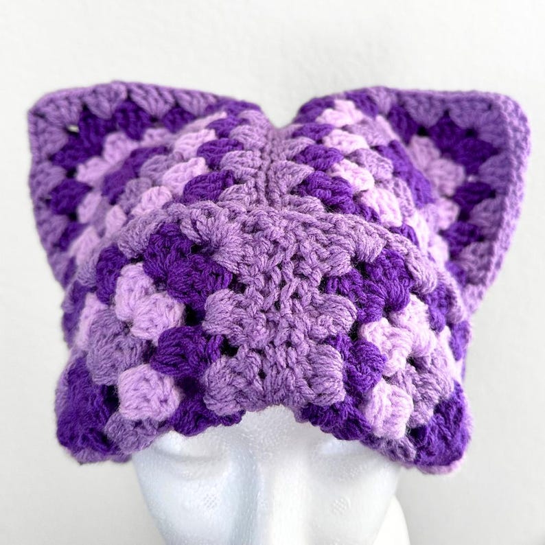May include: Purple and lavender crocheted hat with a square pattern. The hat has a unique shape with two points at the top.