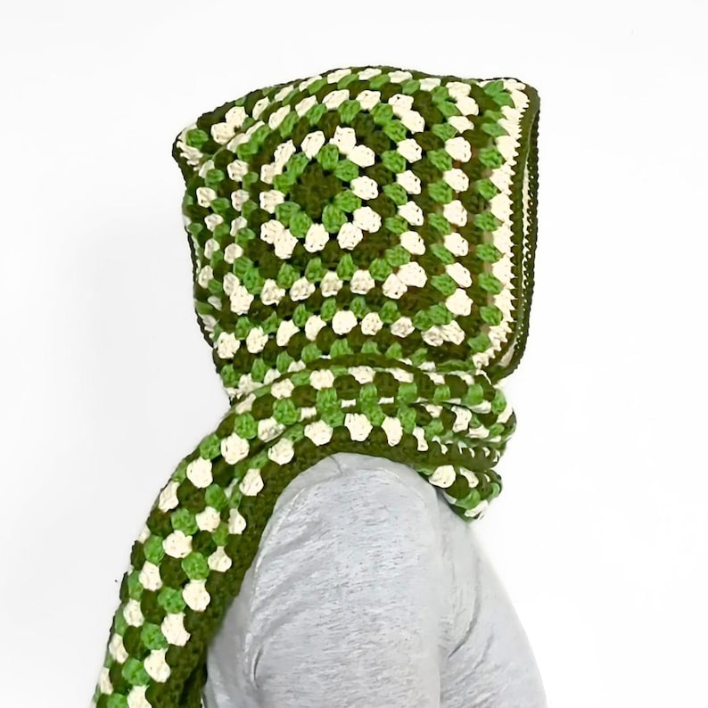 May include: A hooded scarf crafted with a crochet granny square pattern in shades of dark forest green, light lime green, and off-white. The hood features a square construction that transitions into a long, integrated scarf with a matching pattern.