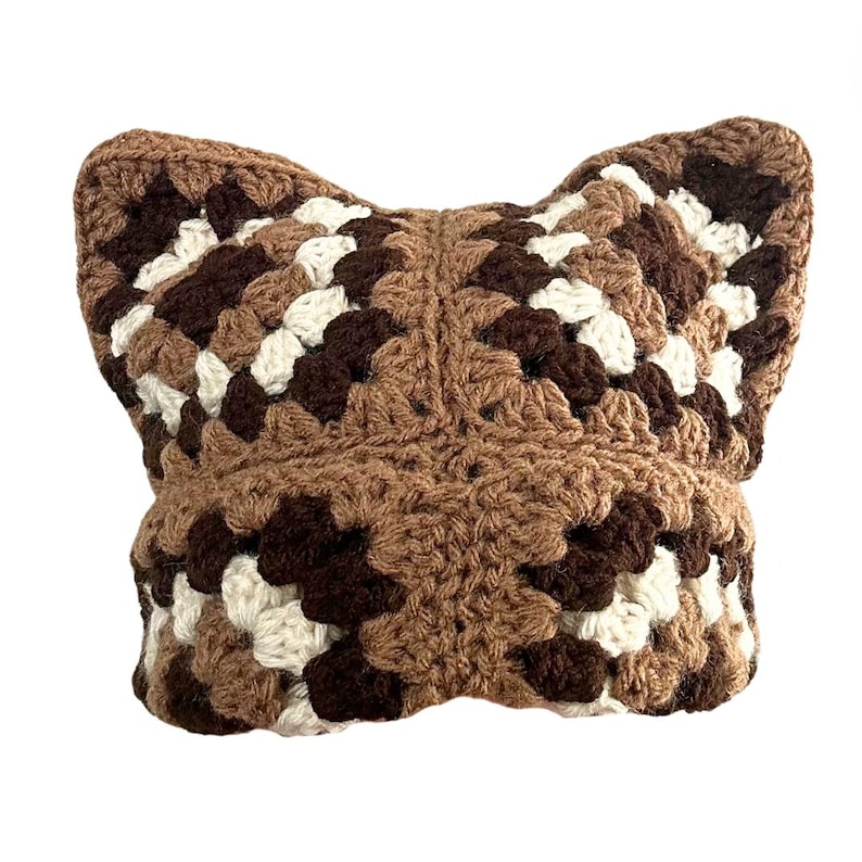 May include: A brown, white, and dark brown crocheted cat hat with large ears.