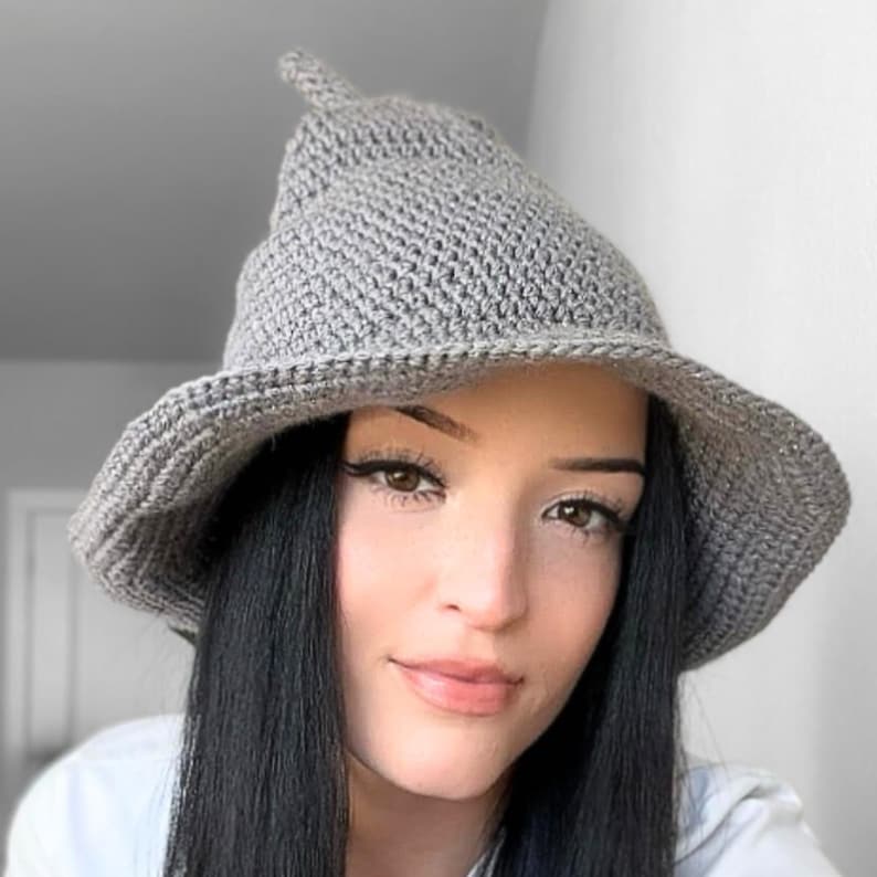 May include: A gray crocheted witch hat with a pointed crown and wide brim. The hat is worn by a person with long black hair.