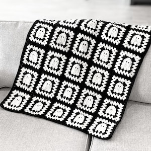 May include: A handmade crochet blanket constructed from square motifs. Each square features a white ghost figure centered within a black and white geometric border. The overall design consists of a repeating pattern of these ghost squares.