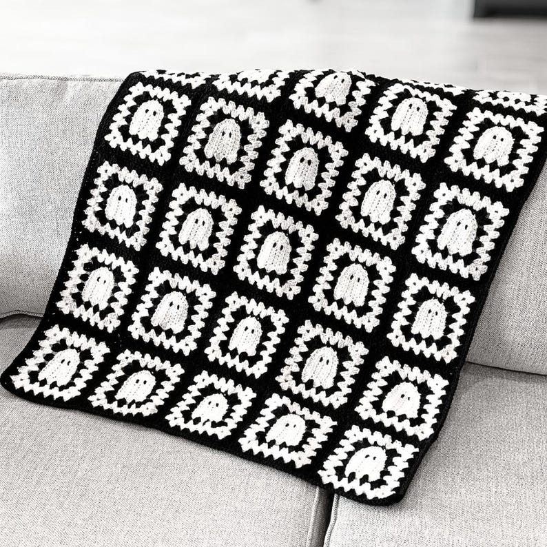 May include: A handmade crochet blanket constructed from square motifs. Each square features a white ghost figure centered within a black and white geometric border. The overall design consists of a repeating pattern of these ghost squares.